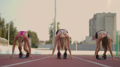 Close-up-three-female-track-and-water-athletes-on-the-start-line-at-the-stadium-competition-prepare-and-run-away-in-a-sprint-race.